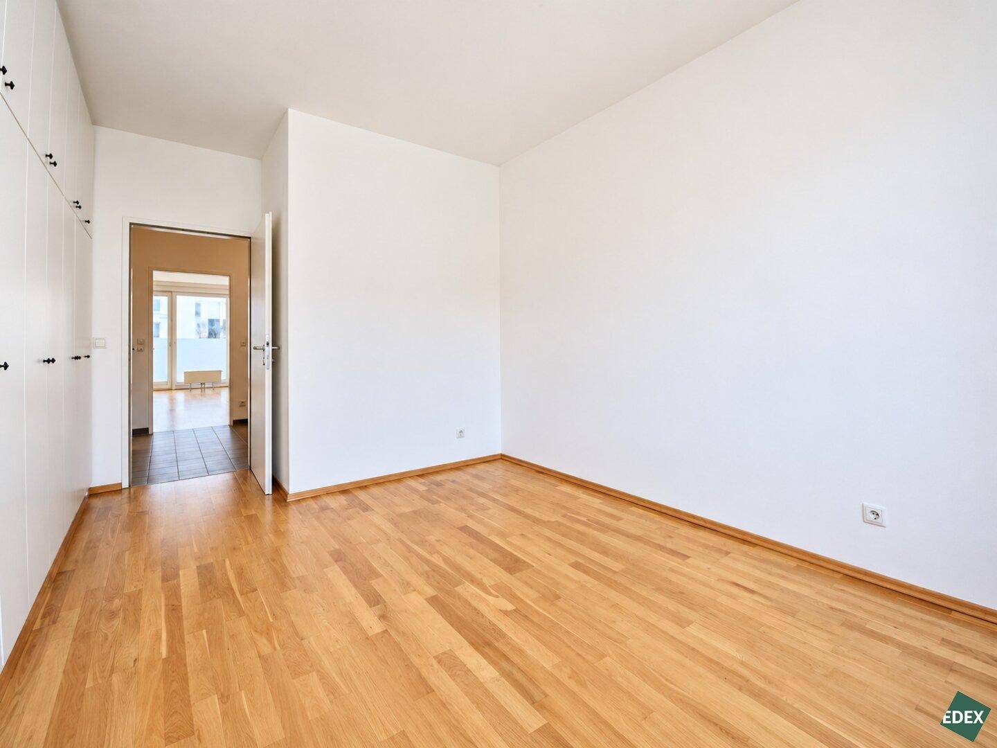 Geräumiges Schlafzimmer mit Parkettboden und integriertem Kleiderschrank, Blick zum Flur.