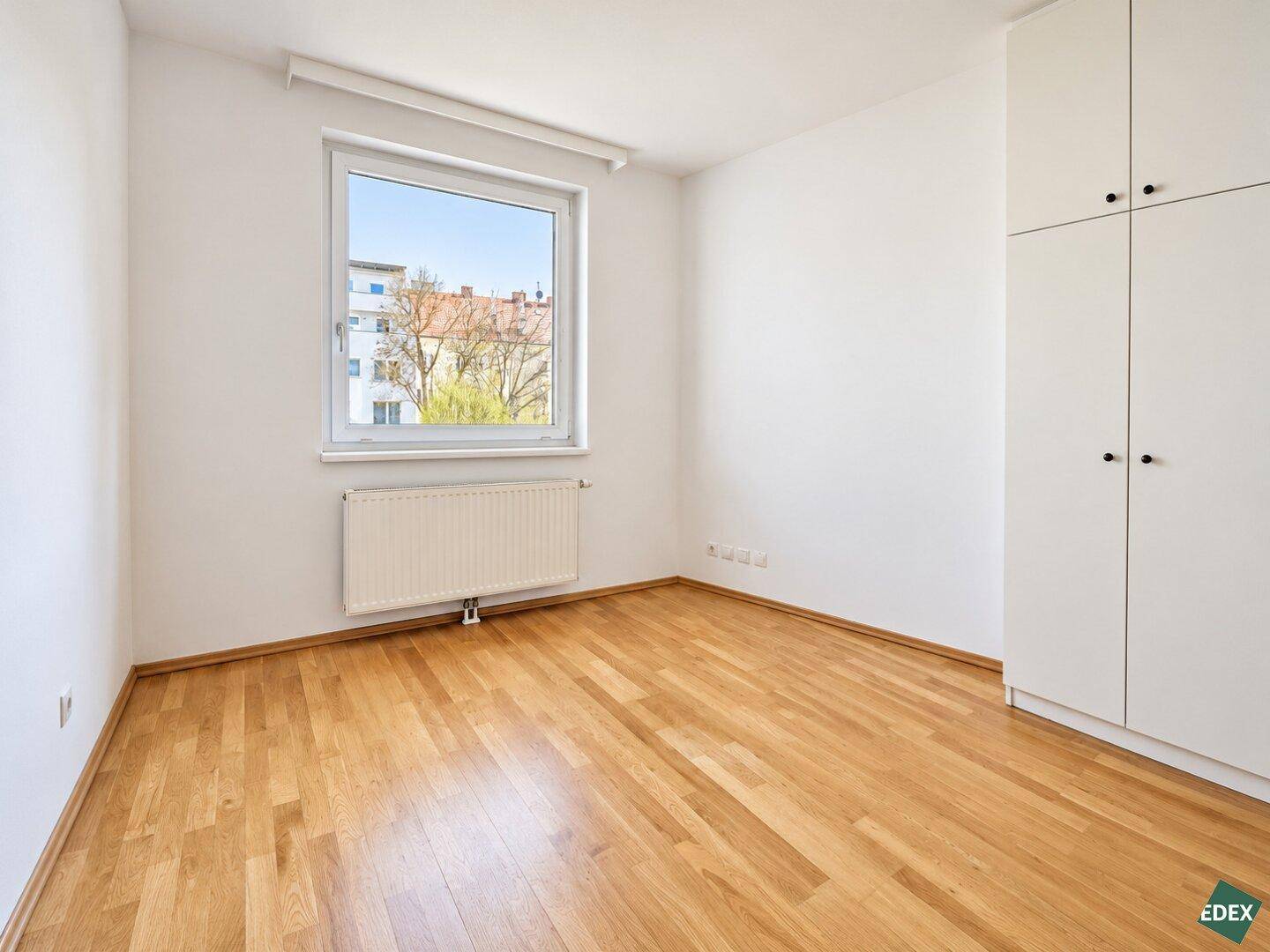 Helles Schlafzimmer mit Parkettboden, großem Fenster und praktischem Einbauschrank.