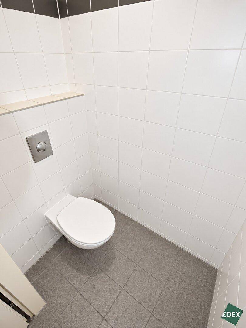 Separates WC mit wandhängender Toilette und weißen Fliesen, sauber und funktional.