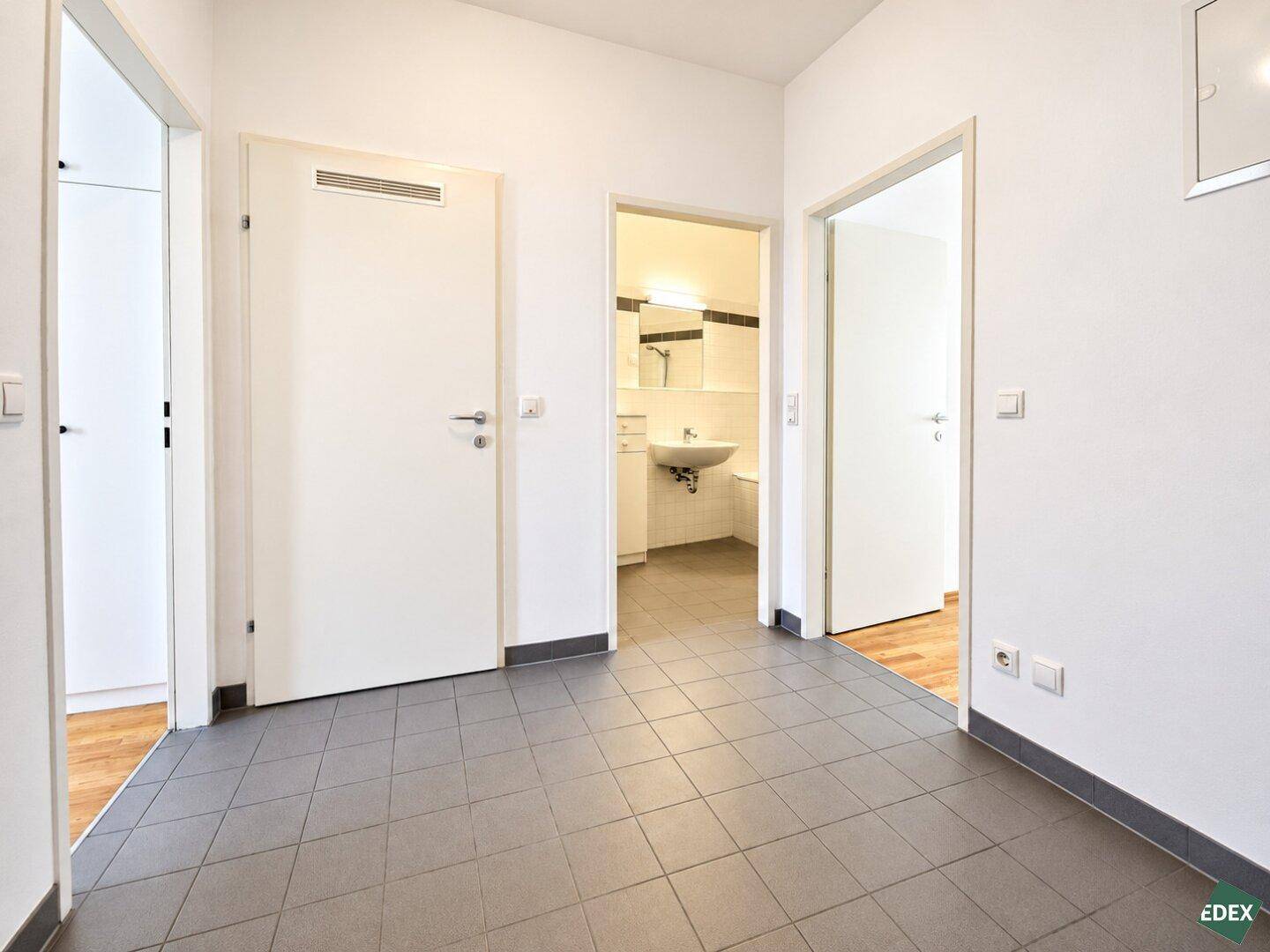 Heller Flur mit grauen Fliesen und Zugang zu verschiedenen Zimmern, inklusive Badezimmer.