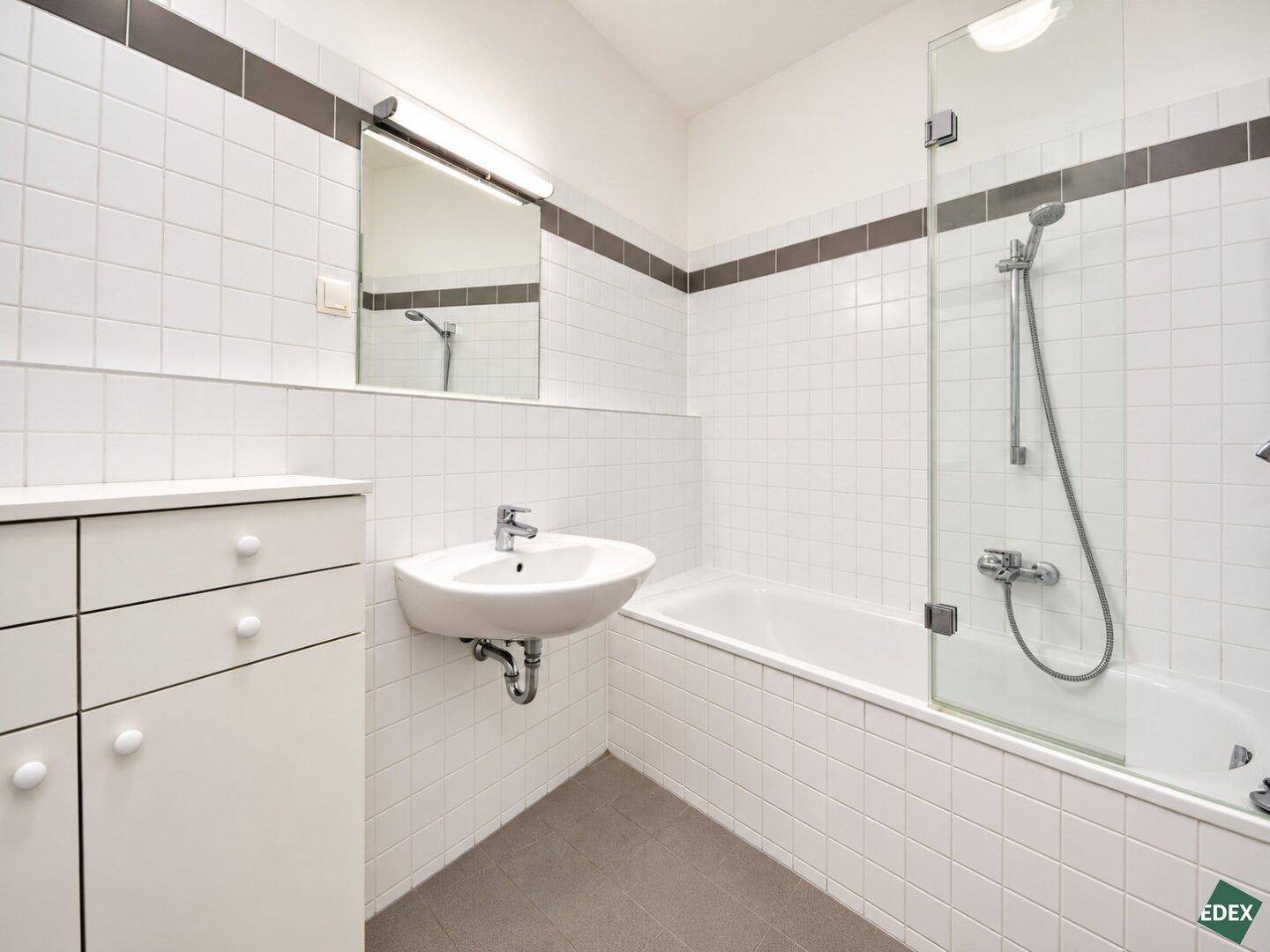 Modernes Badezimmer mit weißen Fliesen, Badewanne mit Duschwand und Einzelwaschbecken.