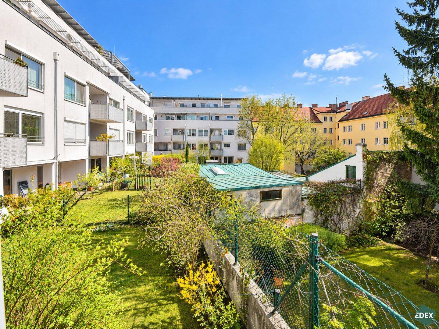Grüne Gartenanlage mit Rasenflächen und Bäumen, umgeben von Wohngebäuden.