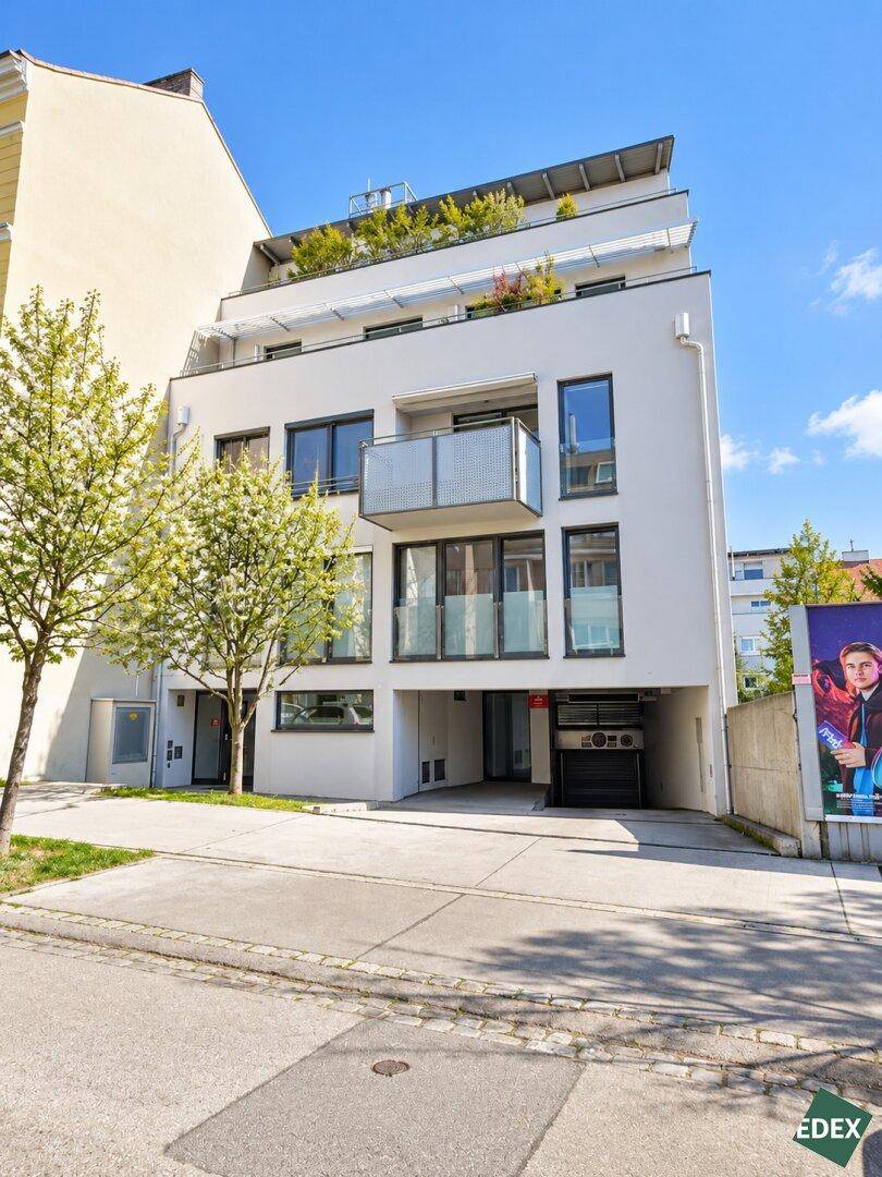 Moderne Gebäudefassade mit Balkonen, großen Fenstern und Zufahrt zur Tiefgarage.