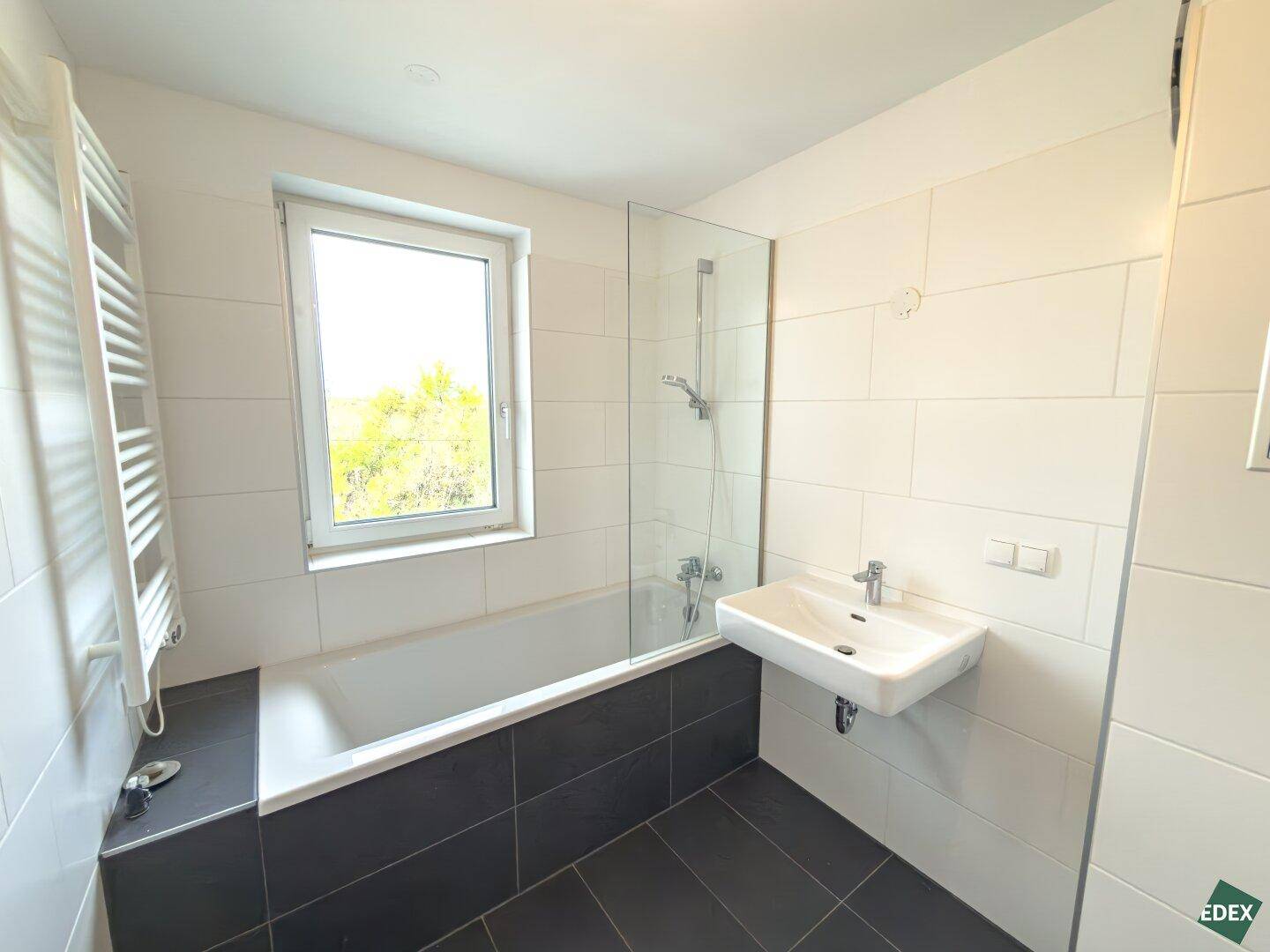 Modernes Badezimmer mit Badewanne, Duschbereich, Einzelwaschbecken und Fenster für Tageslicht.