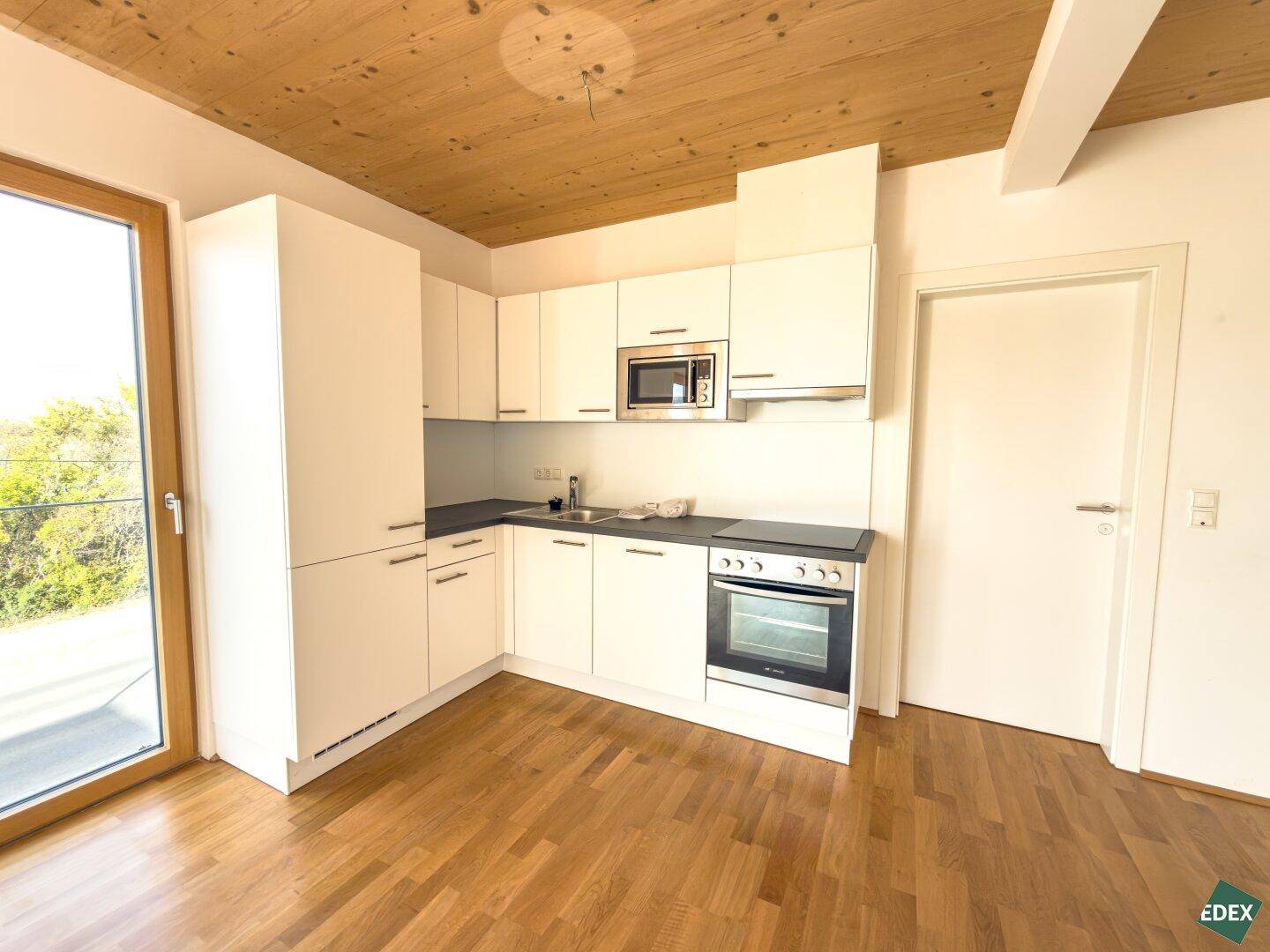 Moderne Küchenzeile mit weißen Schränken, integriertem Backofen und Mikrowelle, sowie Holzboden.