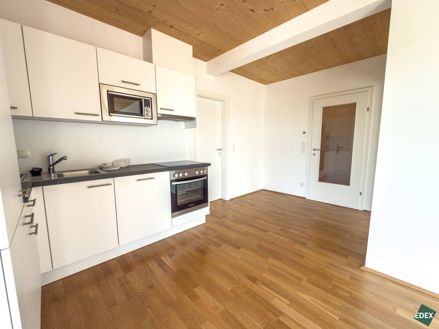 Kompakte Küchenzeile mit weißen Schränken, Backofen und Mikrowelle, ergänzt durch Holzboden.