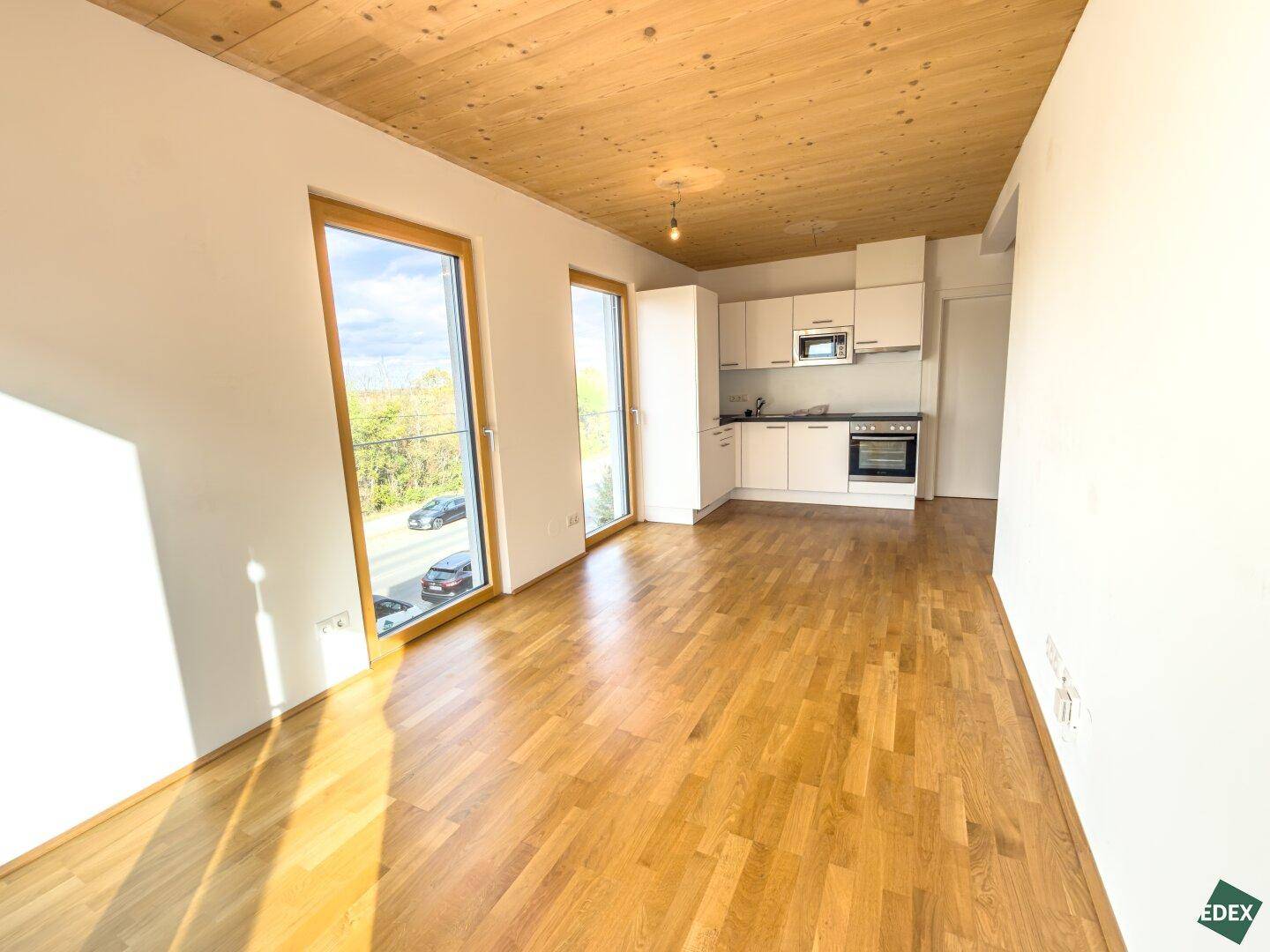 Offener Wohnbereich mit integrierter Küchenzeile, Holzboden und großen Fenstern.