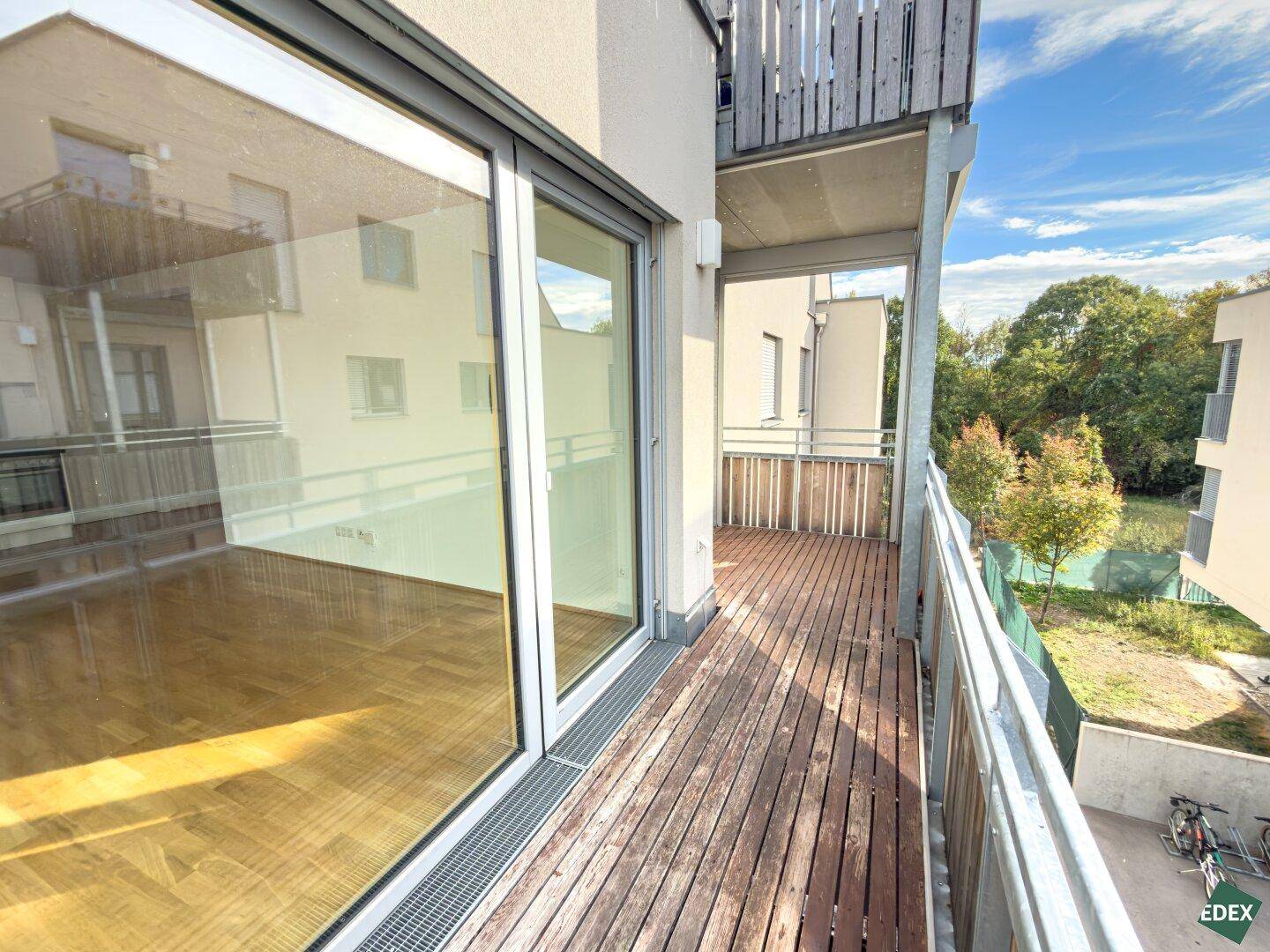 Geräumiger Balkon mit Holzbelag und Blick auf die Umgebung sowie weitere Gebäude.