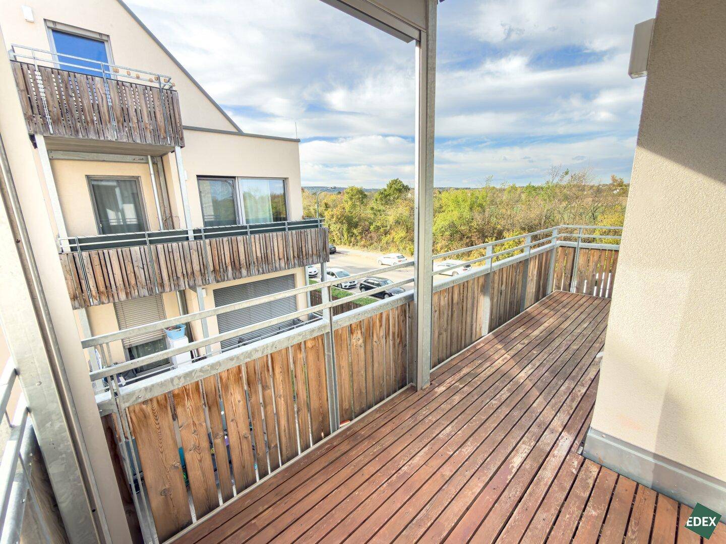 Langer Balkon mit Holzbelag und Blick auf weitere Balkone sowie die umliegende Natur.