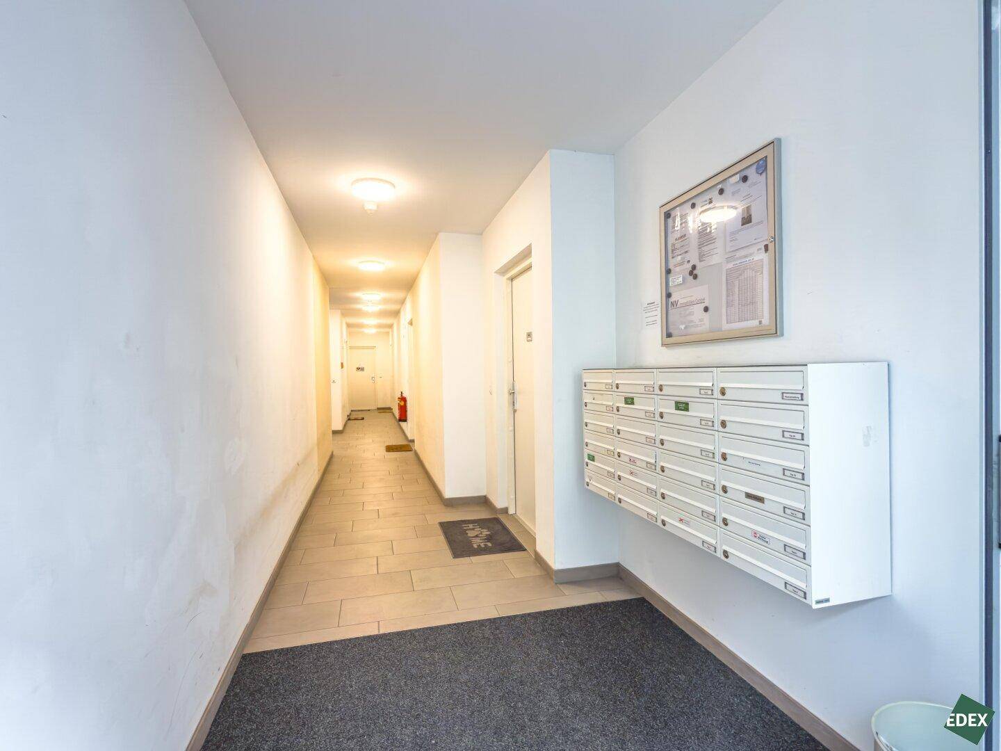 Heller Flur im Gebäude mit Briefkästen an der Wand und Fliesenboden.