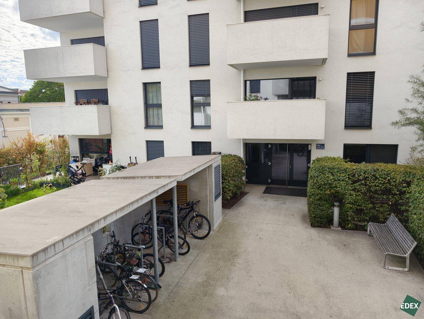 Fahrradabstellplatz unter einem Carport vor dem Eingang eines modernen Wohngebäudes.