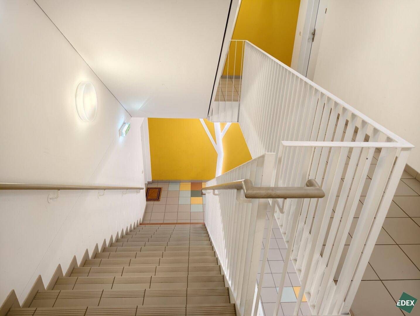 Treppenhaus mit farbigen Akzenten und Fliesenboden in einem Mehrfamilienhaus.