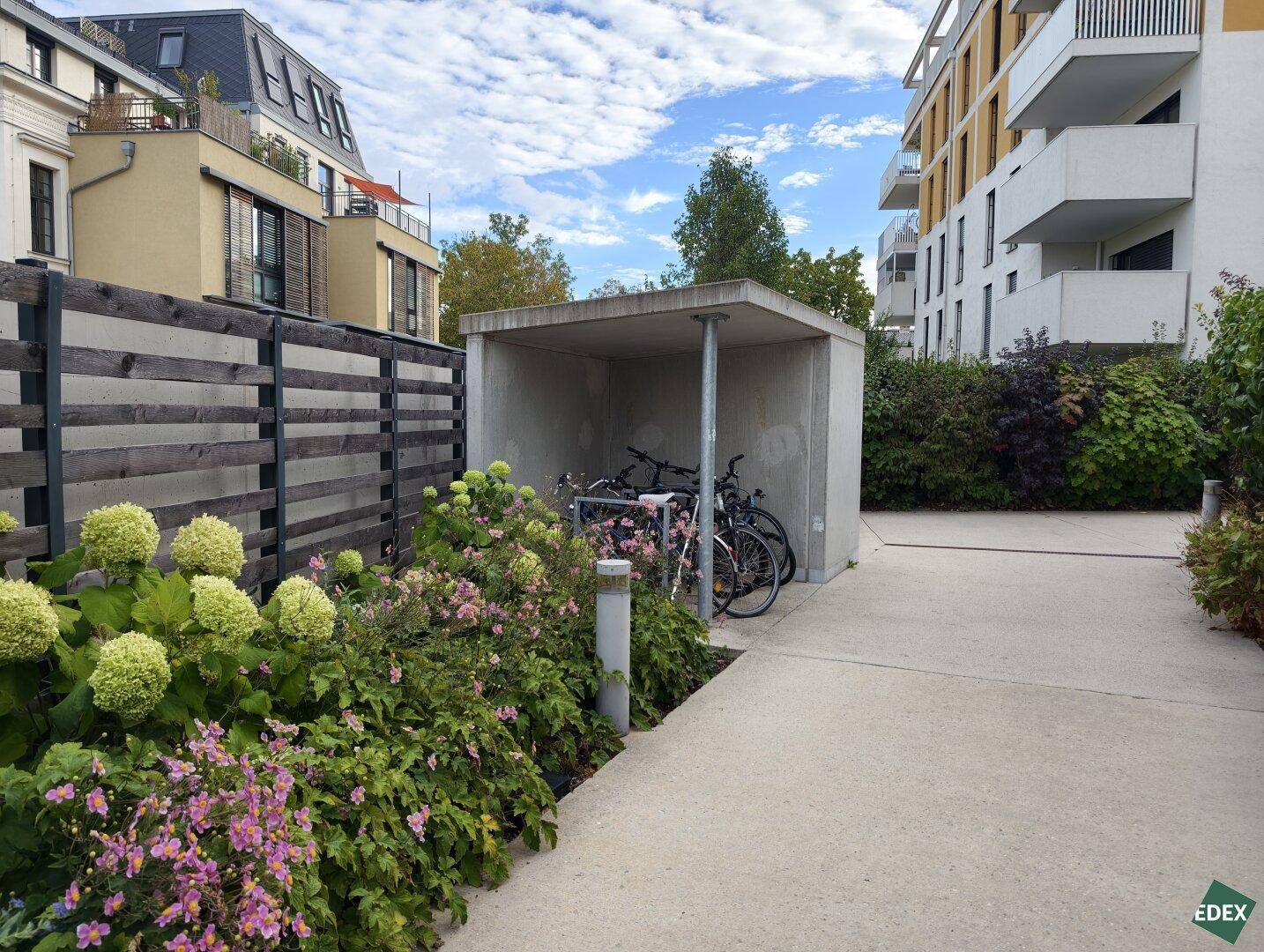 Gepflegter Gartenweg mit Blumenbeeten und einem überdachten Fahrradabstellplatz.