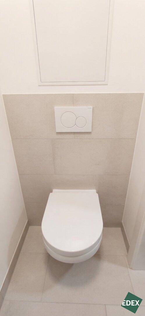 Separates WC mit wandhängender Toilette und hellen Fliesen.