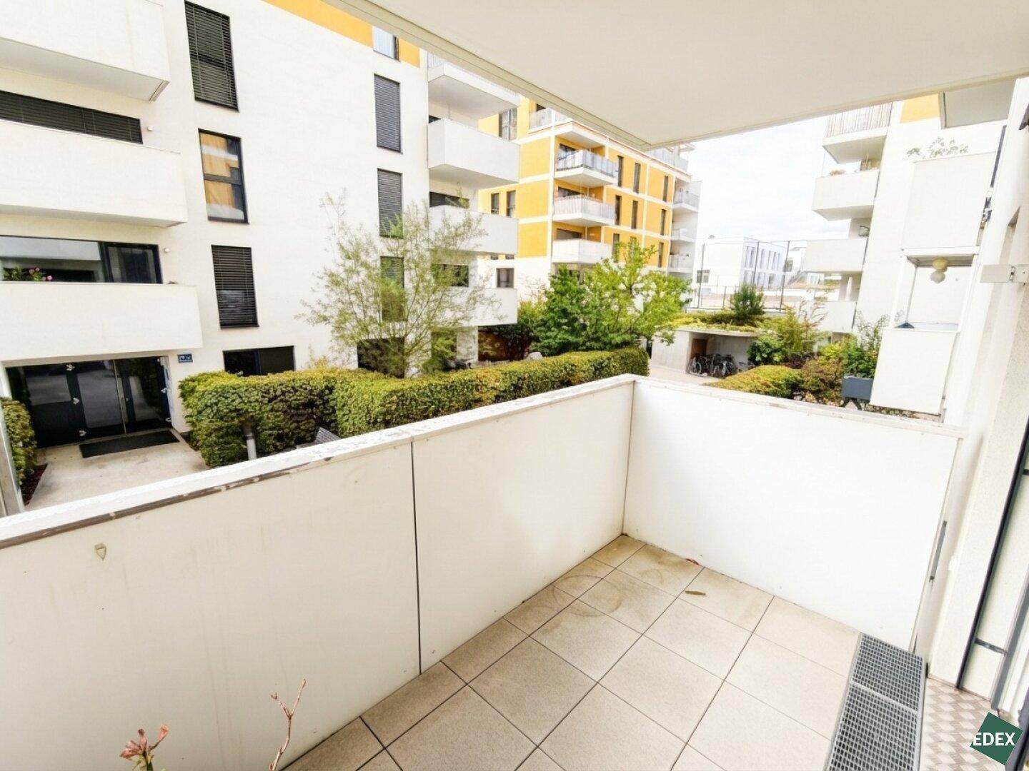 Balkon mit Fliesenboden und Blick auf den begrünten Innenhof der Wohnanlage.