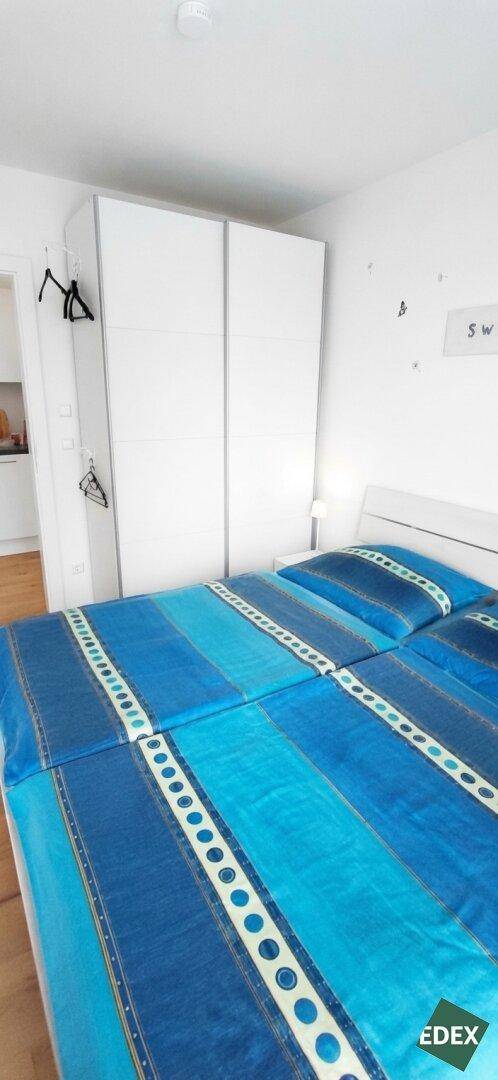 Schlafzimmer mit Doppelbett, blauer Bettwäsche und weißem Kleiderschrank.
