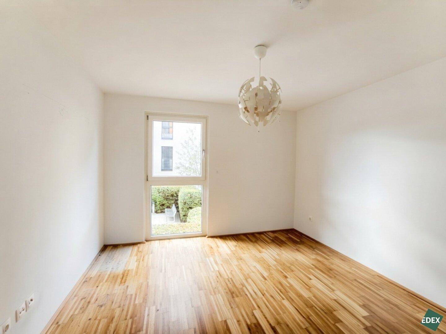 Helles Schlafzimmer mit Parkettboden und Fenster zum grünen Außenbereich.