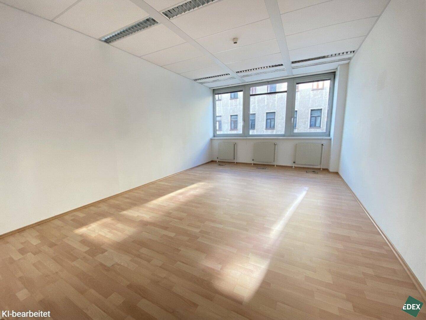 Leeres Büro mit hellem Holzfußboden und Fenstern, die den Raum mit Tageslicht durchfluten.