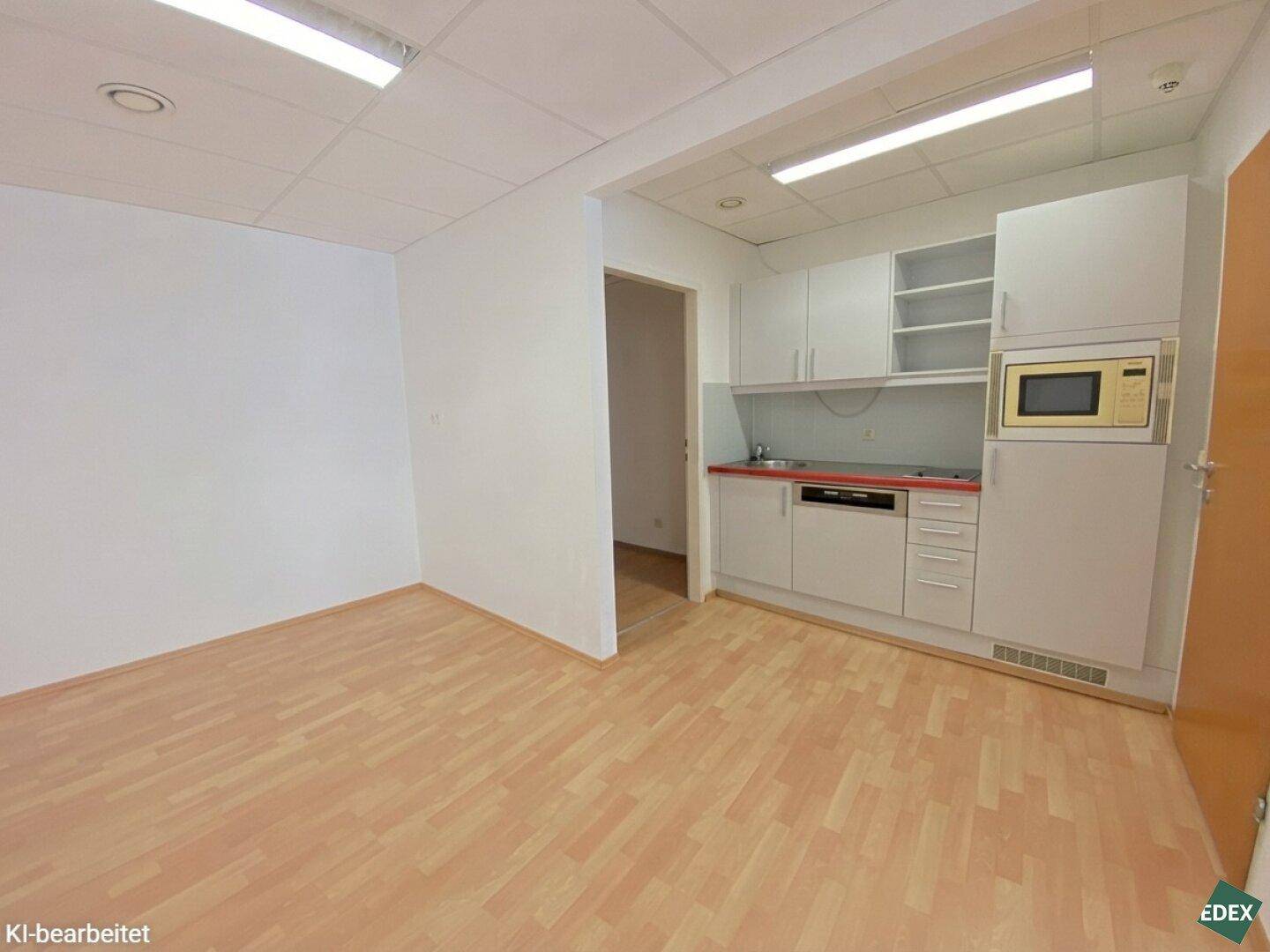 Büroraum mit integrierter Küchenzeile, hellem Holzfußboden und weißen Schränken.