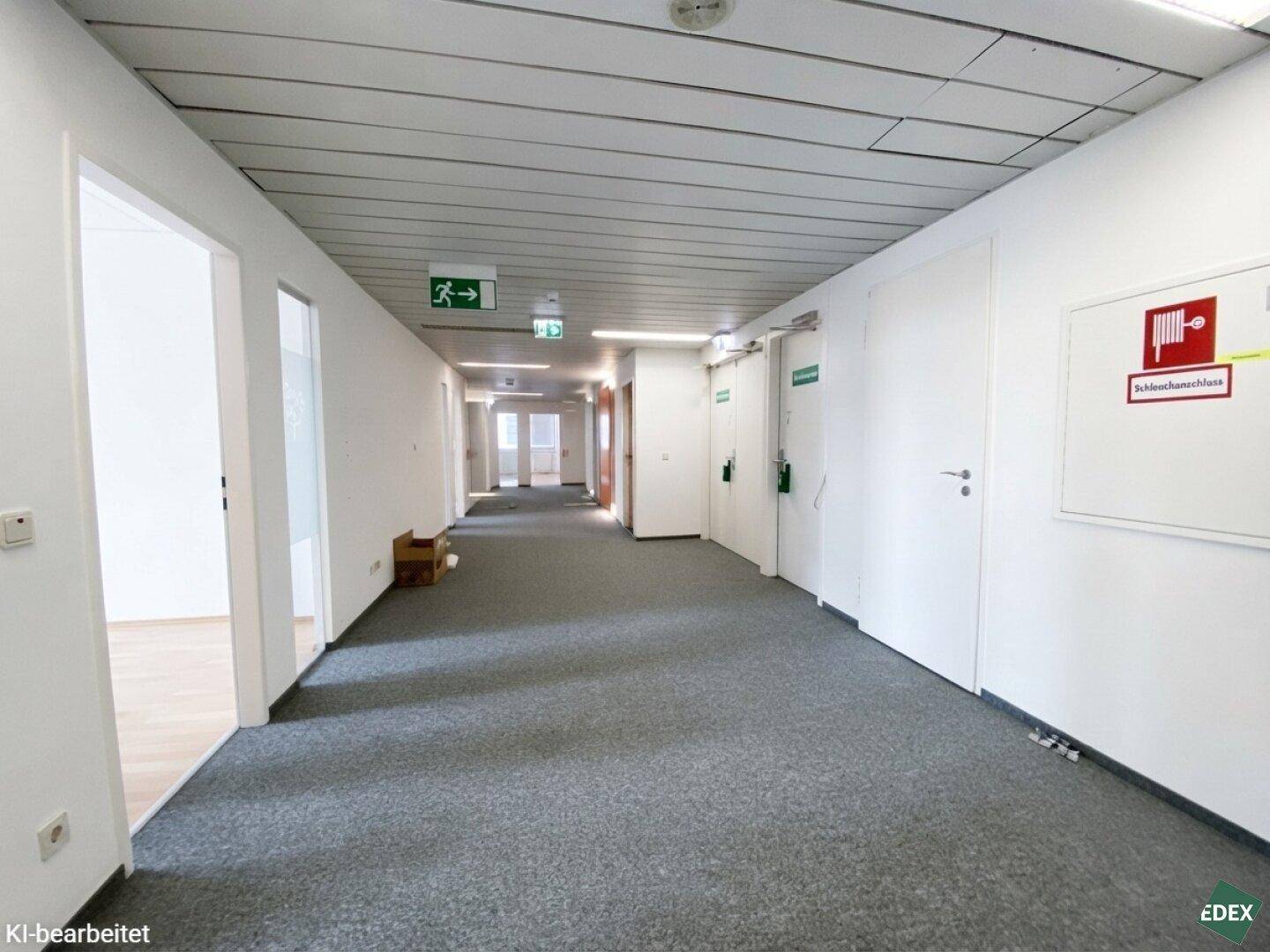 Langer Bürogang mit grauem Teppichboden, weißen Wänden und mehreren Türen zu den Büroräumen.