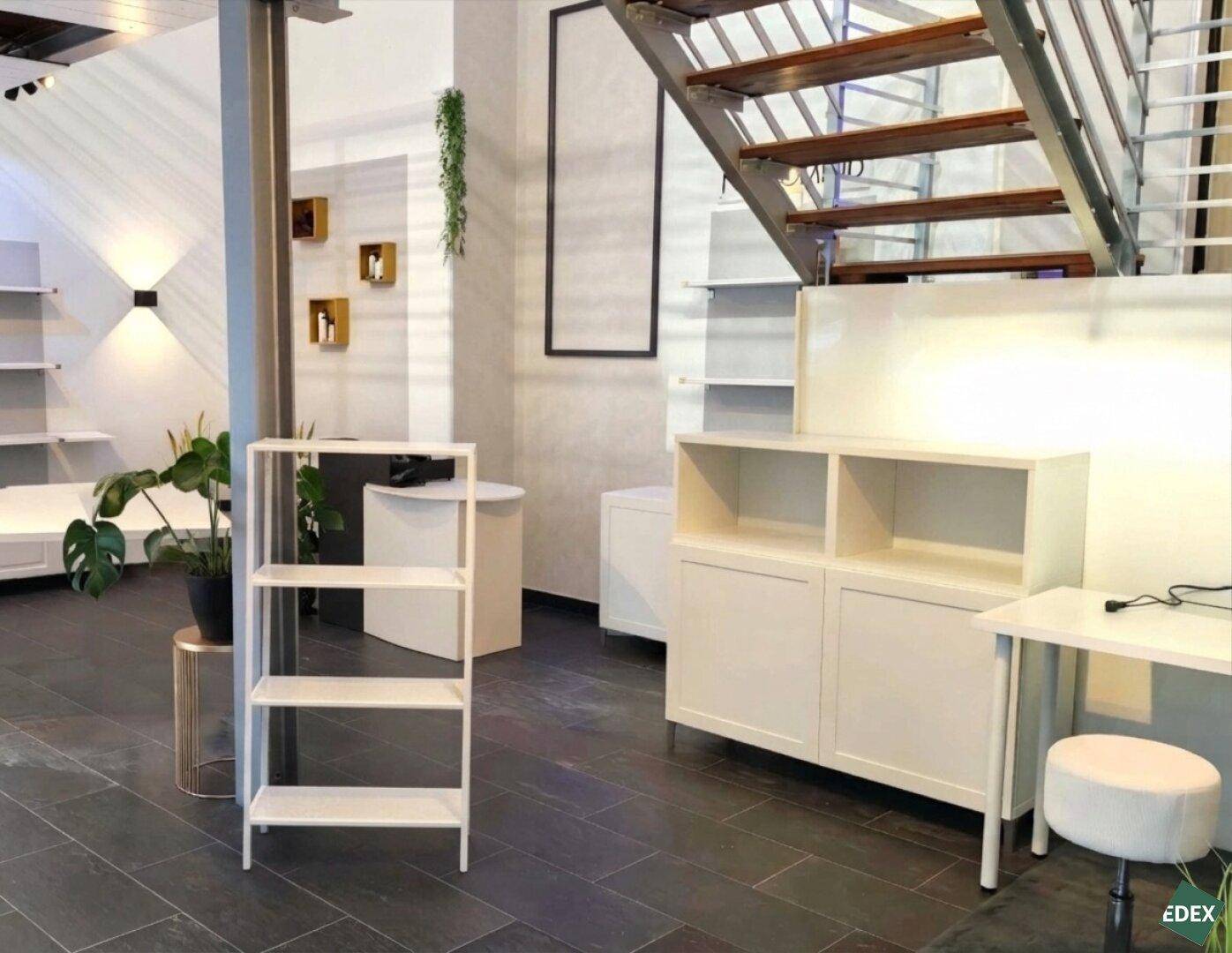Heller Gewerberaum mit dunklem Fliesenboden, offener Treppe und modernen Regalen.