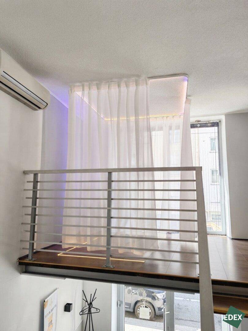 Mezzanine-Bereich mit transparenter Vorhangabtrennung, Holzfußboden und Blick nach draußen.