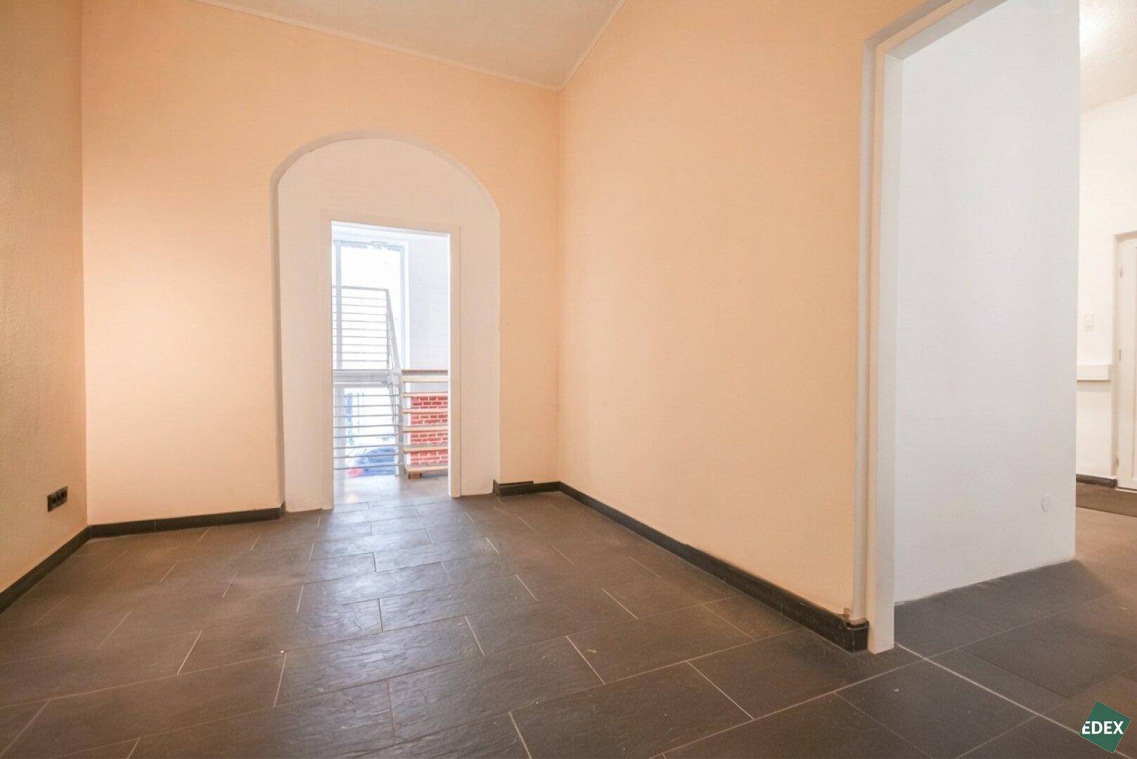 Leerer Raum mit pfirsichfarbenen Wänden, dunklem Fliesenboden und einem Rundbogen-Durchgang.