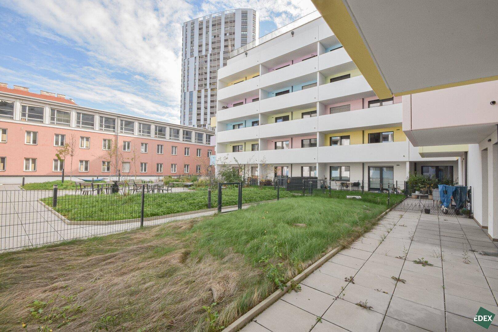 Gemeinschaftsgartenbereich mit Rasenflächen und Sitzgelegenheiten zwischen modernen Gebäuden.