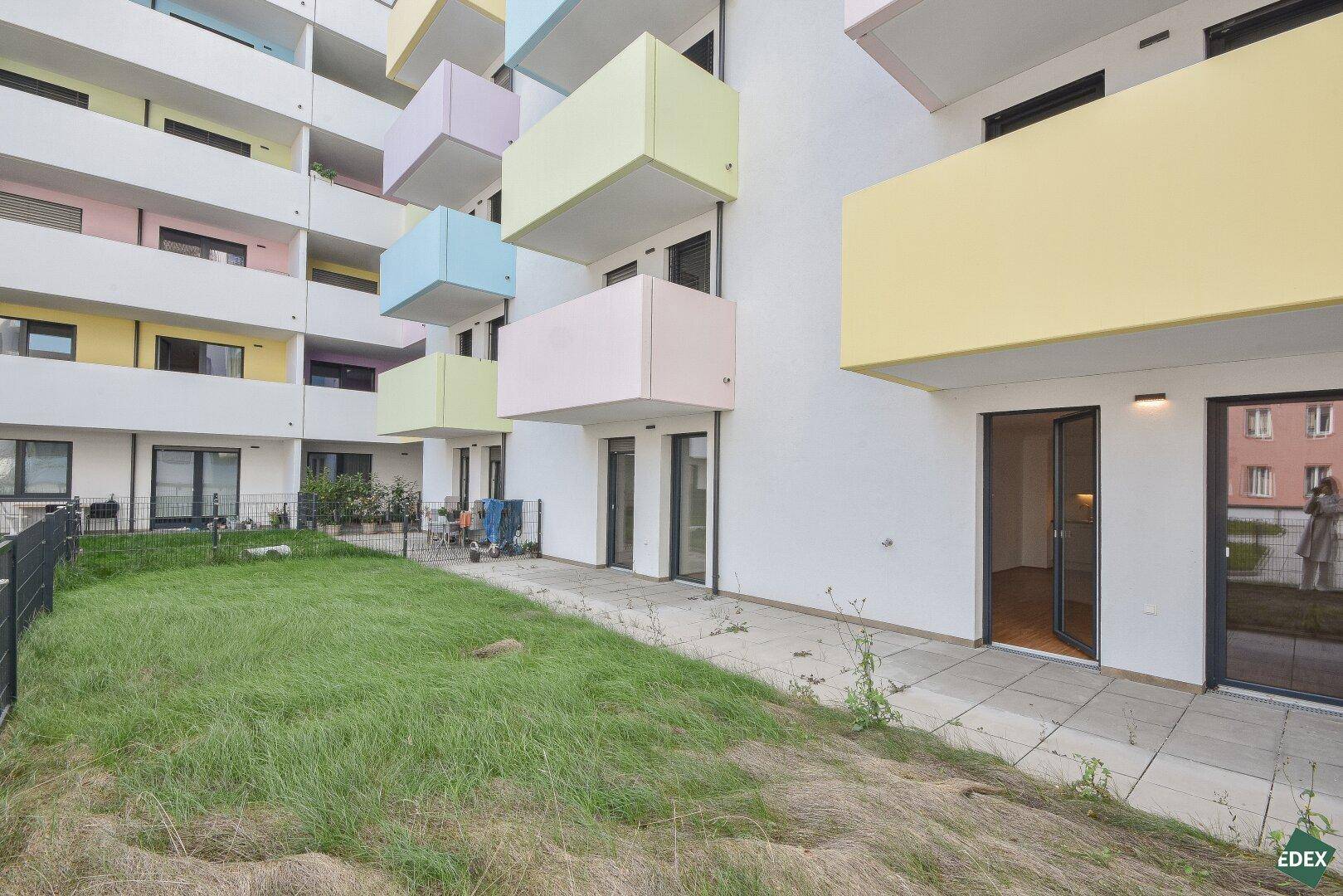 Blick auf den Gemeinschaftsgarten und die farbenfrohen Balkone eines modernen Wohngebäudes.