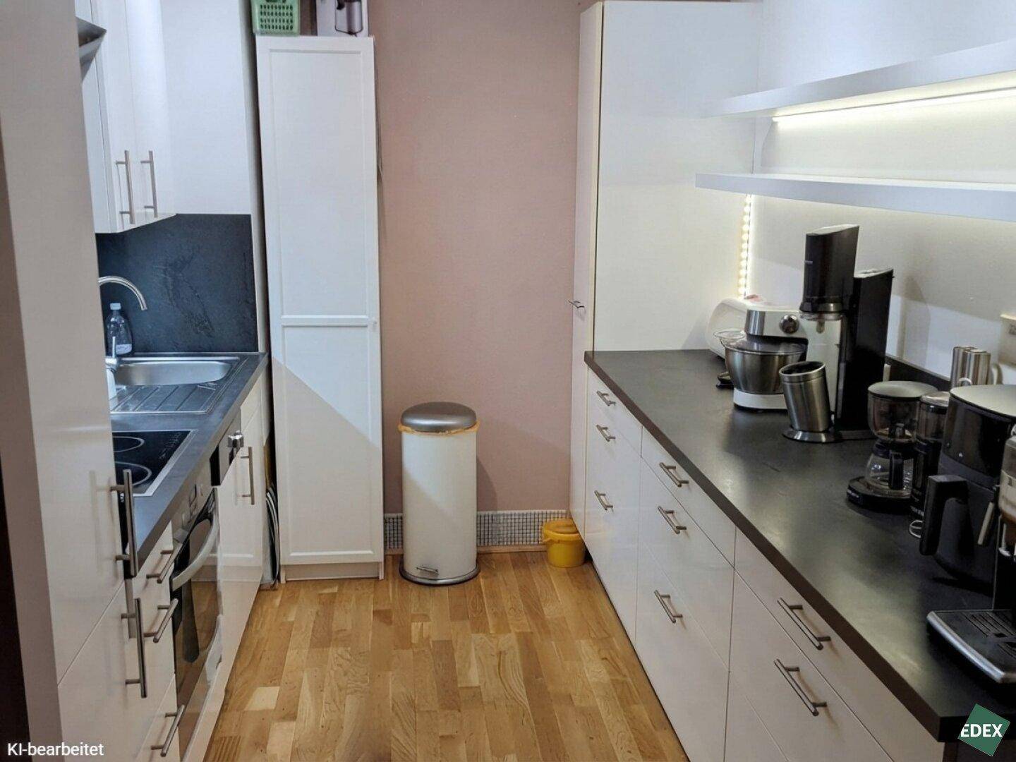 Schmale Küche mit weißen Schränken, dunkler Arbeitsplatte und Holzboden.