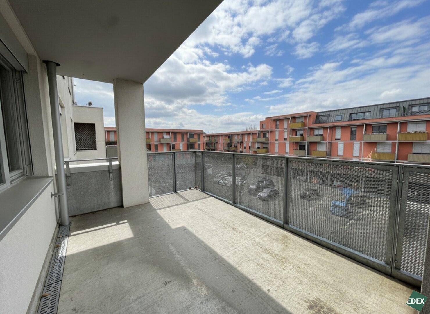 Geräumiger Balkon mit Metallgeländer und Blick auf die umliegenden Gebäude und den Parkplatz.