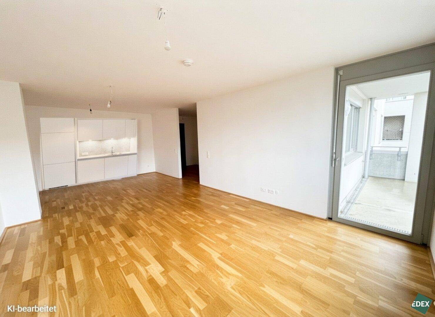 Offener Wohnbereich mit integrierter Küche, Parkettboden und Zugang zu einem Balkon.