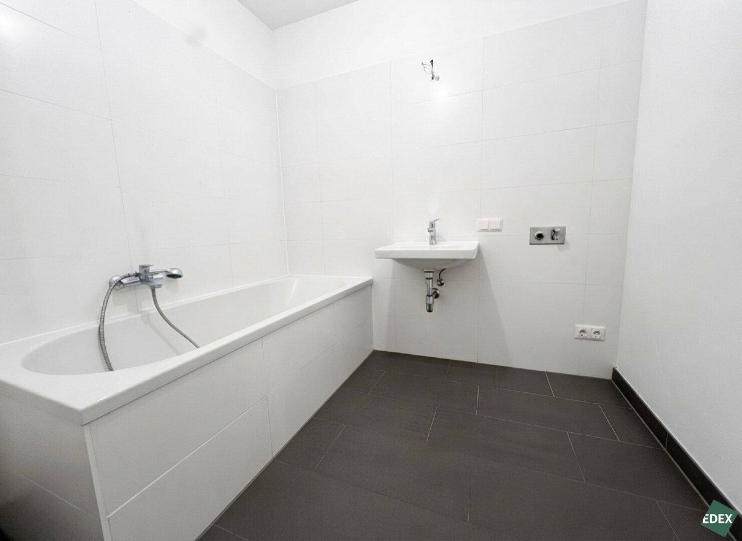 Modern gefliestes Badezimmer mit Badewanne, Waschbecken und dunklem Fliesenboden.