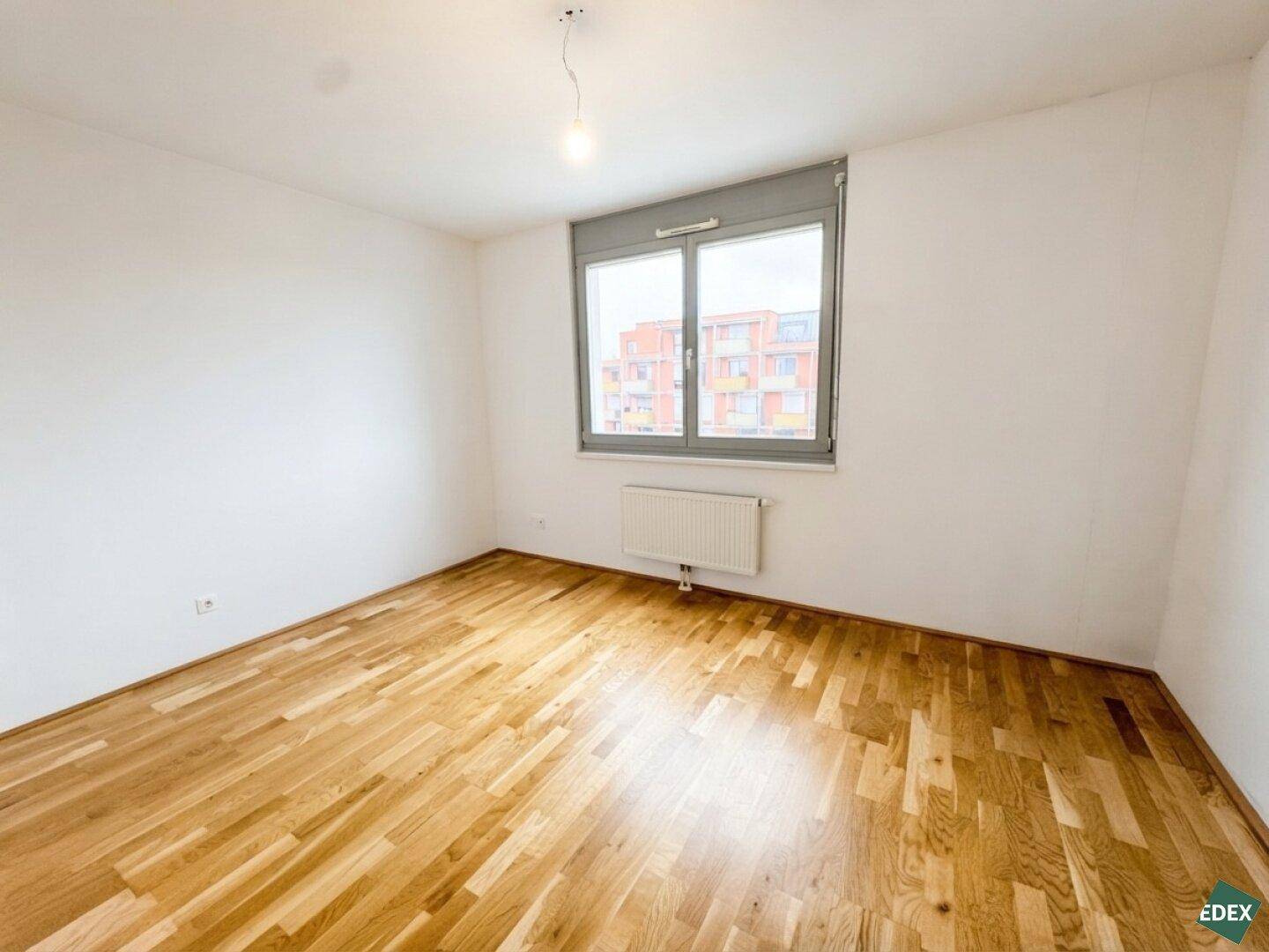 Helles Schlafzimmer mit Parkettboden, weißen Wänden und einem großen Fenster.