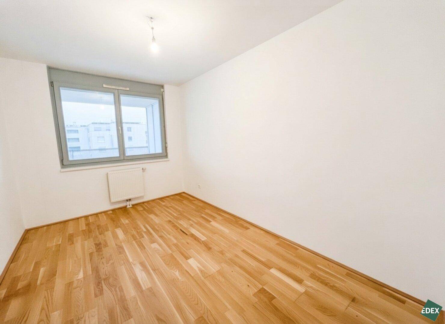 Weiteres helles Zimmer mit Parkettboden und Fenster, ideal als Schlaf- oder Arbeitszimmer.