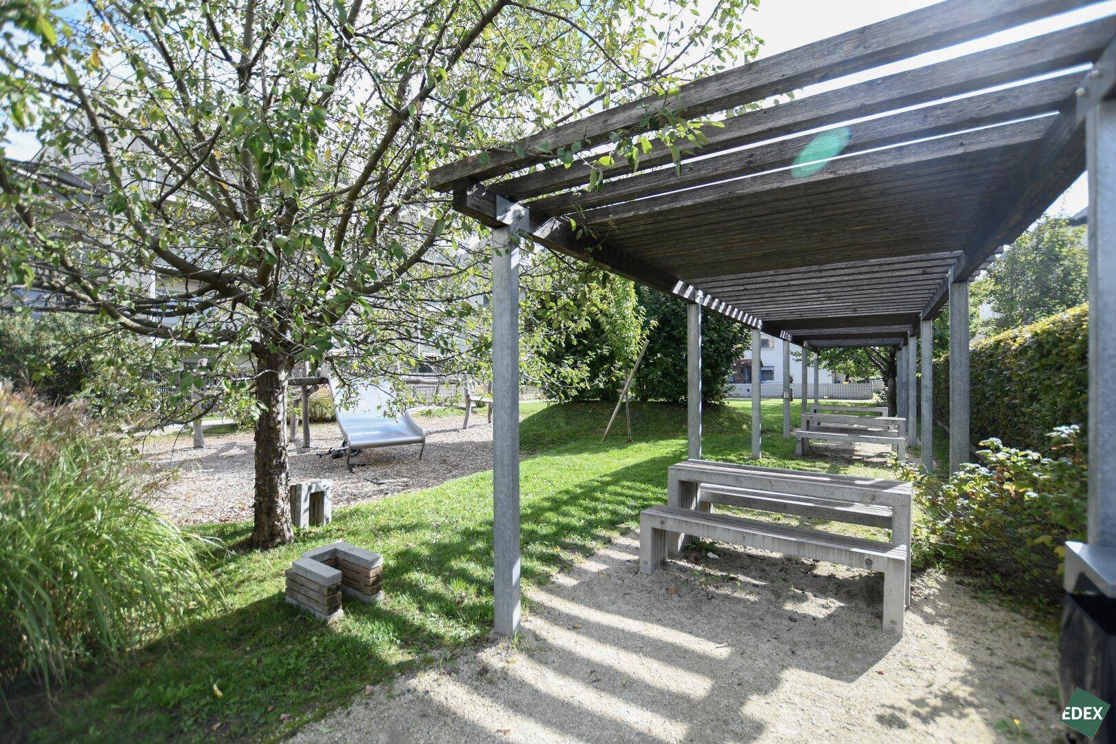 Gemeinschaftlicher Gartenbereich mit Pergola, Sitzgelegenheiten und einem Spielplatz für Kinder.