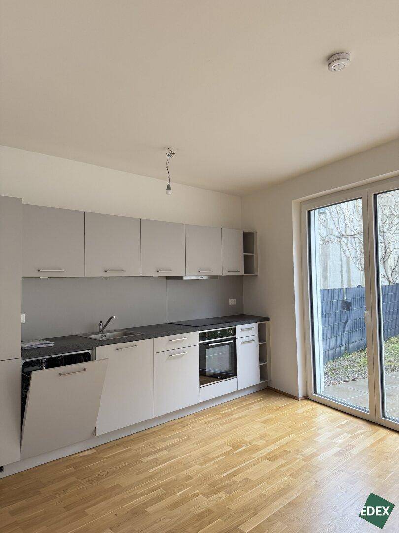 Moderne Einbauküche in Grau mit integrierten Geräten und Blick ins Grüne.