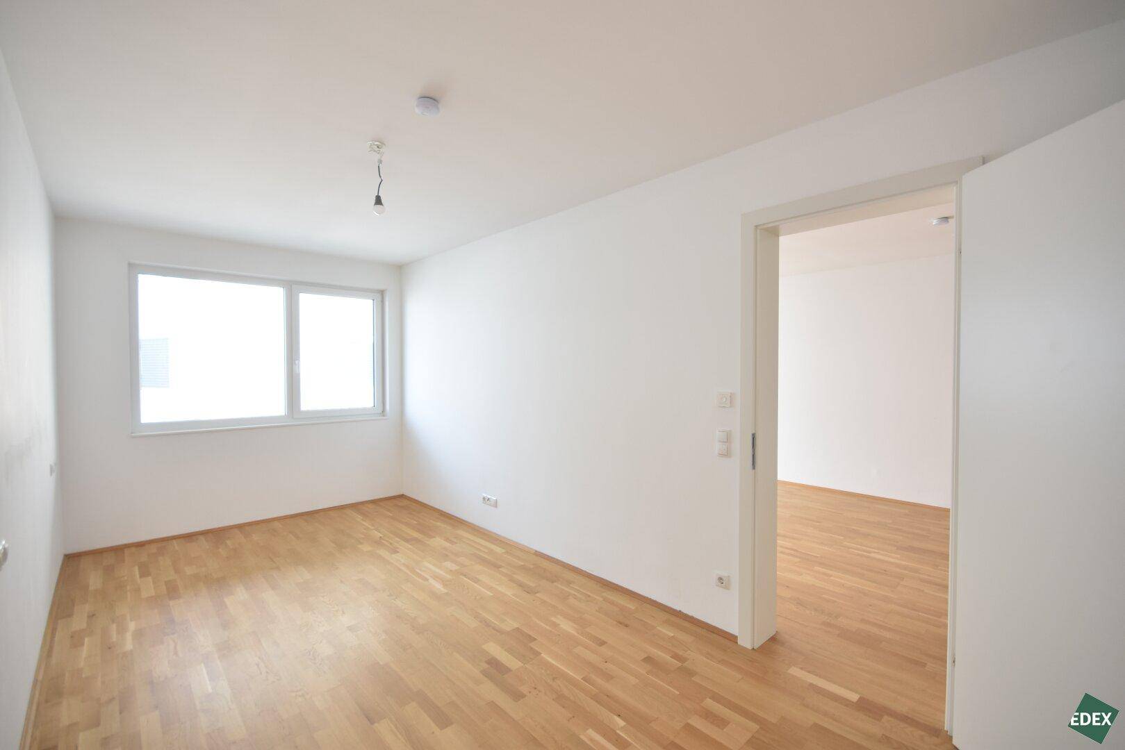 Helles Schlafzimmer mit Parkettboden und großem Fenster, bereit zur Einrichtung.
