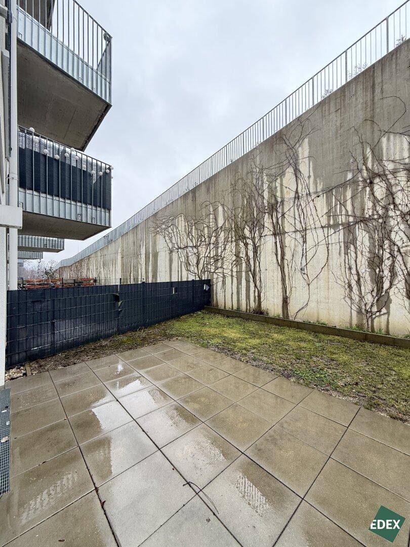 Geflieste Terrasse mit kleinem Gartenanteil und Blick auf eine begrünte Wand.