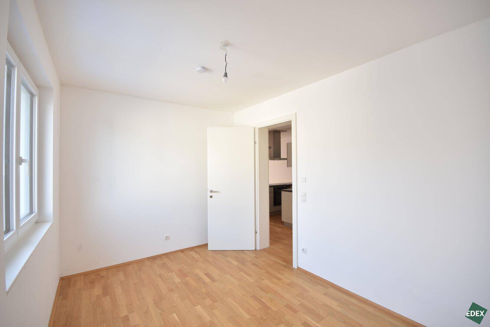 Heller, leerer Raum mit Parkettboden und Fenster, bereit zur individuellen Gestaltung.