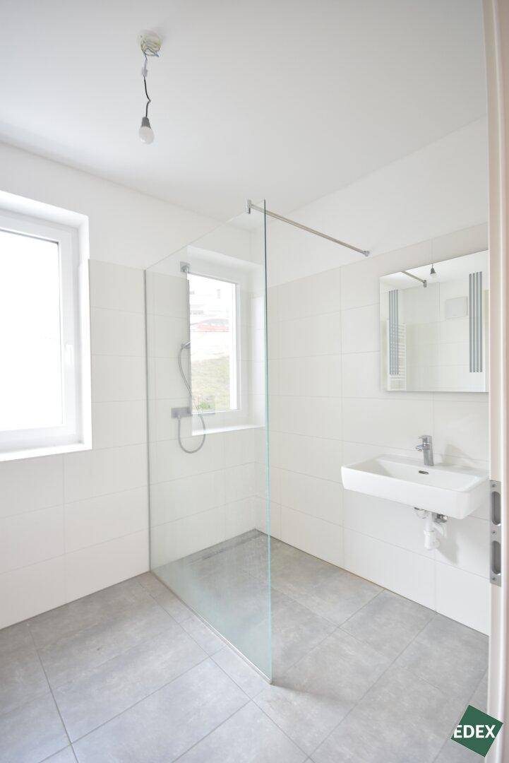 Modernes Badezimmer mit ebenerdiger Dusche, Fenster und weiß-grauen Fliesen.