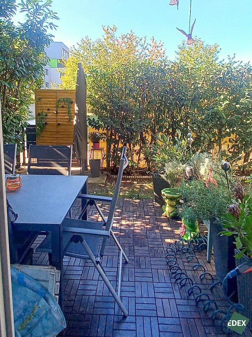 Sonnige Terrasse mit Holzbodenfliesen, Esstisch und üppiger Bepflanzung, ideal für Mahlzeiten im Freien.