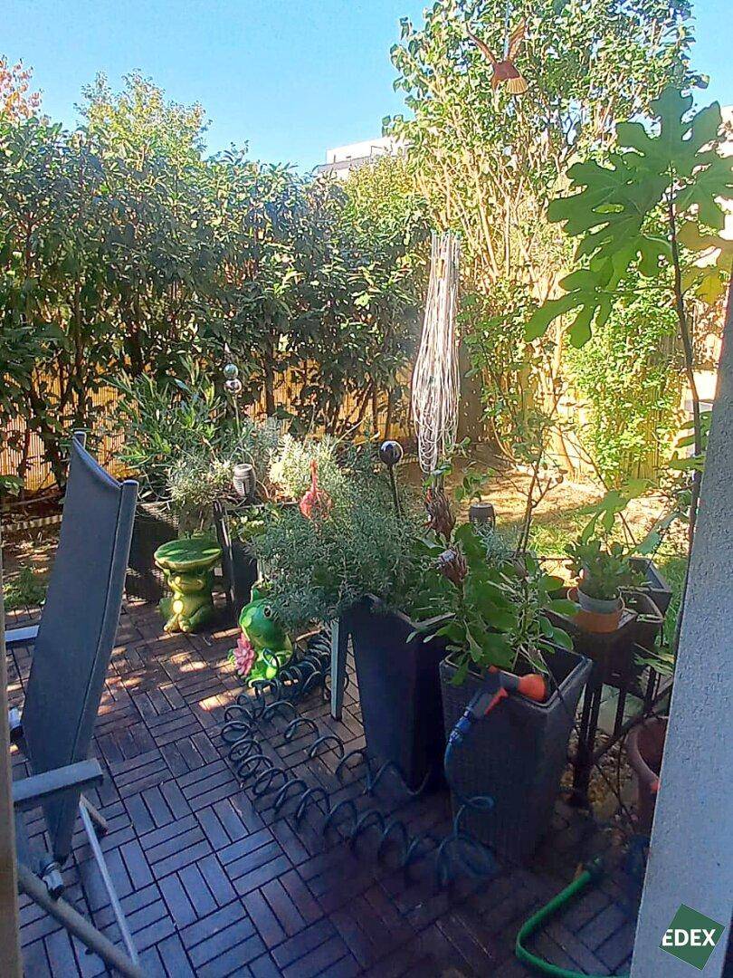 Gemütliche Terrasse mit vielen Pflanzen und Sitzgelegenheiten, umgeben von grünen Hecken und Bäumen.