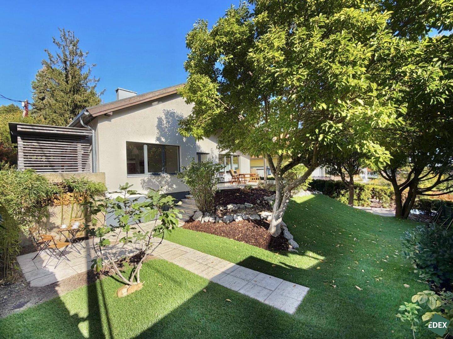 Gepflegter Gartenbereich mit Rasen, Bäumen und einer kleinen Terrasse neben dem Haus.