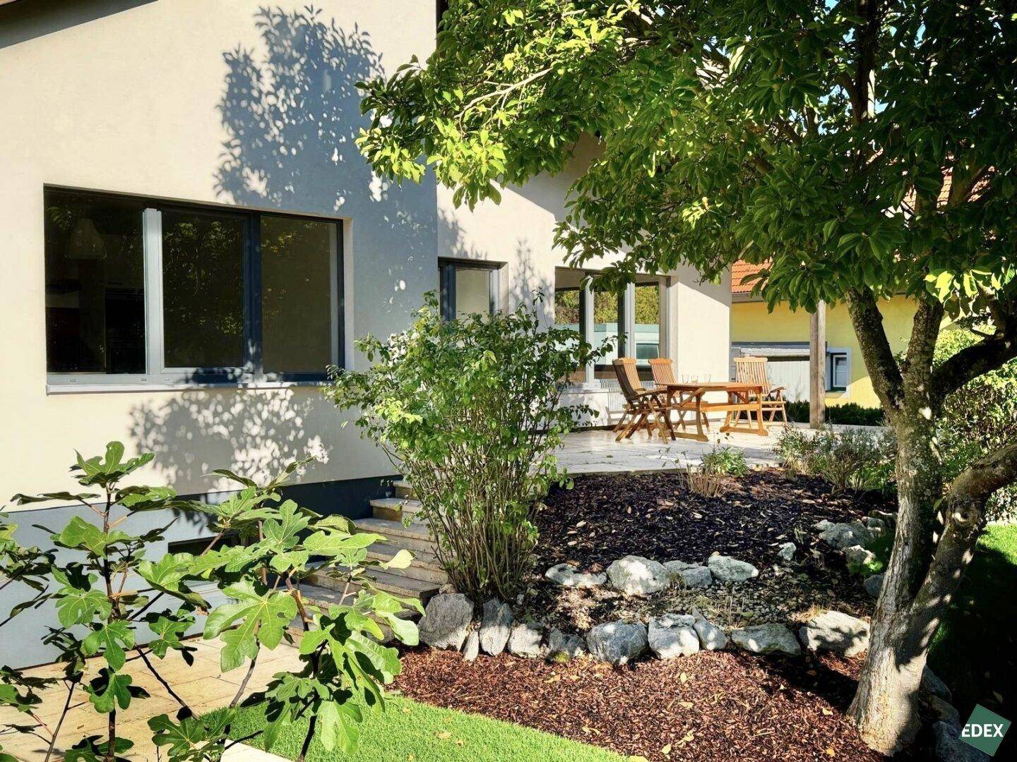 Sonniger Terrassenbereich mit Gartenmöbeln und umgebender Bepflanzung am Haus.