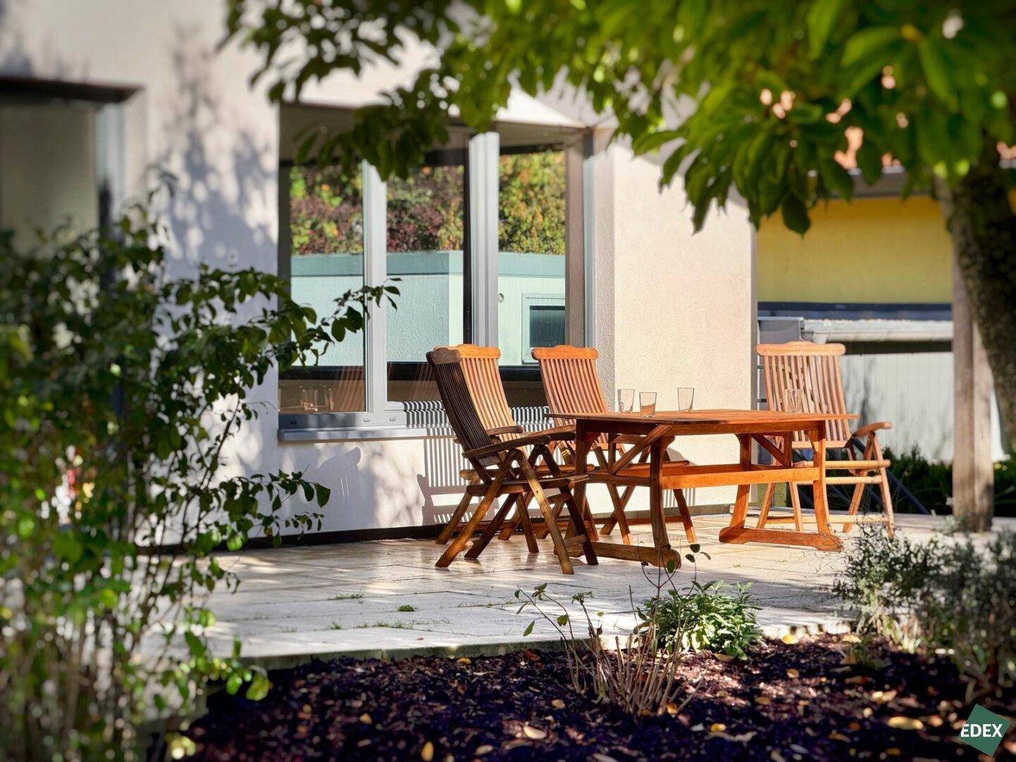 Gemütlicher Terrassenbereich mit Holztisch und Stühlen, umgeben von grüner Natur.