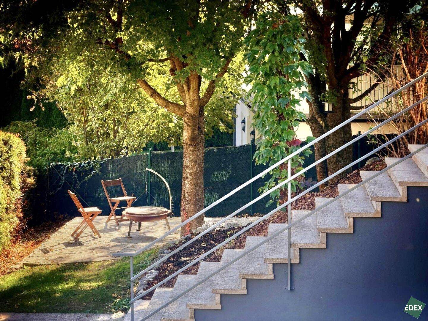 Steintreppe führt zu einem gepflasterten Bereich mit Feuerstelle und Sitzgelegenheiten im Garten.