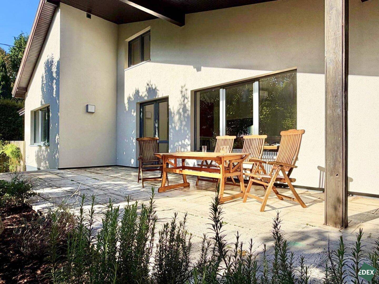 Großzügige, gepflasterte Terrasse mit Holzmöbeln und Blick auf die grüne Umgebung.