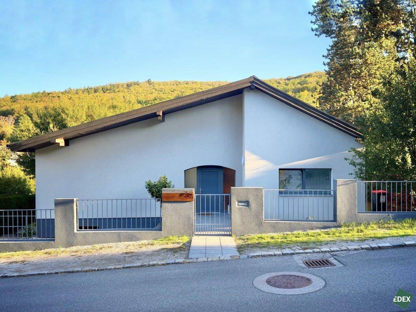 Vorderansicht des Hauses von der Straße mit Zaun, Tor und gepflegtem Vorgarten.