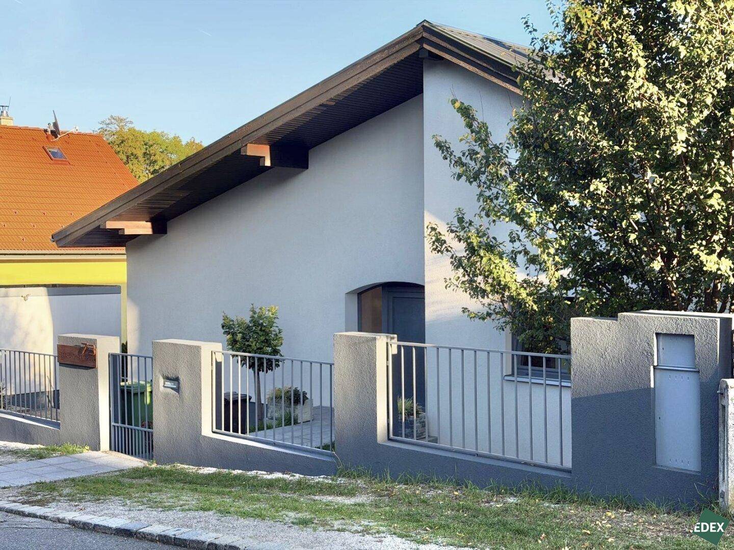 Vorderansicht des Hauses mit modernem Zaun und Tor, umgeben von Grünflächen.
